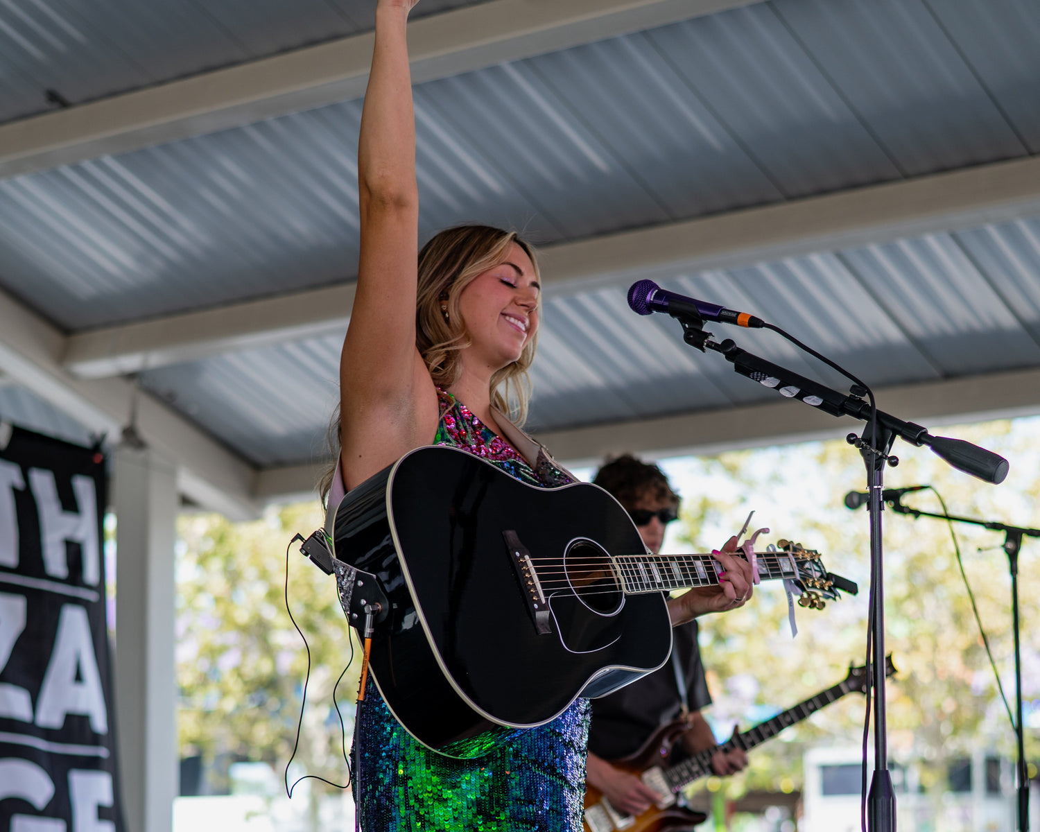 Alli Brown smiling on stage with her guitar in hand and arm in the air
